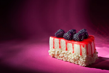 Cake with black raspberries on a pink background. Triangular piece of cake on a paper background. Sweets close up.