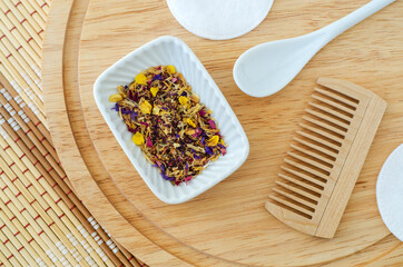 Small white bowl with dried flowers and herbs and wooden hairbrush. Natural skin and haircare, homemade spa and beauty treatment recipe. Herbal medicine, zero waste concept. Top view, copy space.