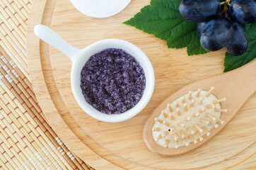 Small white bowl with homemade grape and sugar body scrub (foot soak) and wooden hairbrush. Natural beauty treatment and spa recipe. Top view.