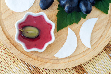 Small bowl with red grape juice (vinegar, extract, tincture) and cotton eye patches. Ingredients for preparing diy eye or face mask. Natural beauty treatment and spa recipe. Top view, copy space.