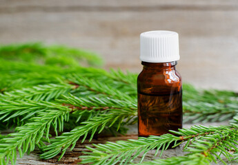 Small glass bottle with essential fir oil, fir branches close up. Aromatherapy, sauna, homemade spa and herbal medicine ingredients. Copy space.