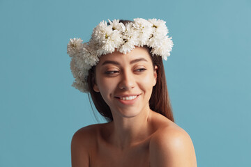 Pretty charming girl in wreath of flowers posing isolated over blue color studio background....