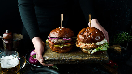 Set of delicious burgers on an old board in the hands of a chef. On a dark background.