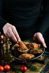 Baked buffalo chicken wings on a plate in the hands of a chef on a black background.
