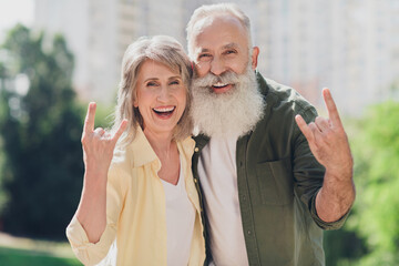 Photo of funky cool senior couple wear casual clothes walking showing hard rock sign smiling...