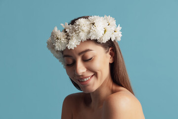 Pretty charming girl in wreath of flowers posing isolated over blue color studio background. Natural beauty concept.