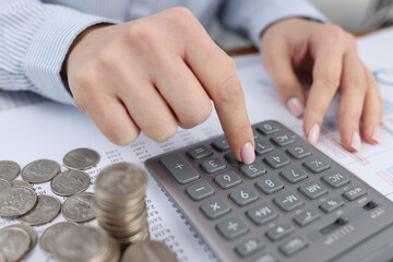 Woman counting on calculator at table with documents and coins closeup