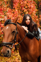 Beautiful girl in the autumn in the forest with a brown horse