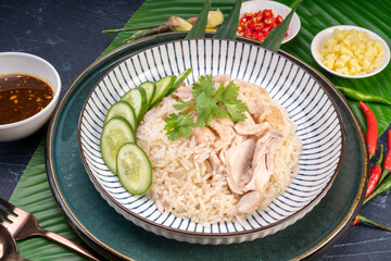 Steamed rice topped with chicken on banana leaves, Hainanese chicken rice served with chili sauce on a wooden background.
