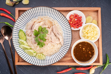 Steamed rice topped with chicken on wooden background, Hainanese chicken rice served with chili...