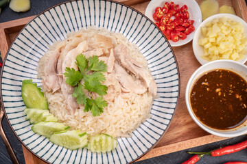 Steamed rice topped with chicken on wooden background, Hainanese chicken rice served with chili sauce on a wooden background.