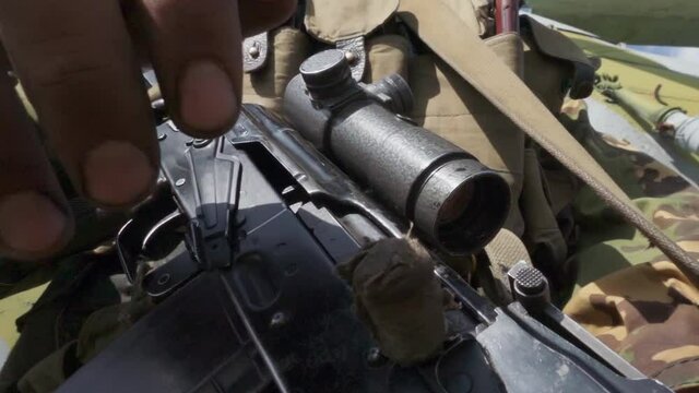Man in Combat Camouflage and Body Armor Disengages the Safety on his Rifle and Cocking the Bolt Carrier. Soldier sends a cartridge to the chamber on a modern machine