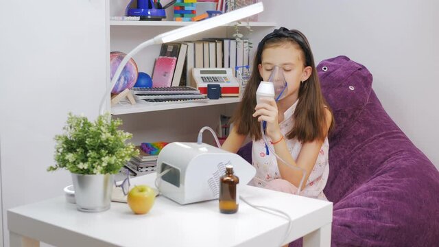 Portrait of cute child is sick bronchitis or asthma and breathe through inhaler at home Little girl makes inhalation with medical nebulizer while sitting at the table.