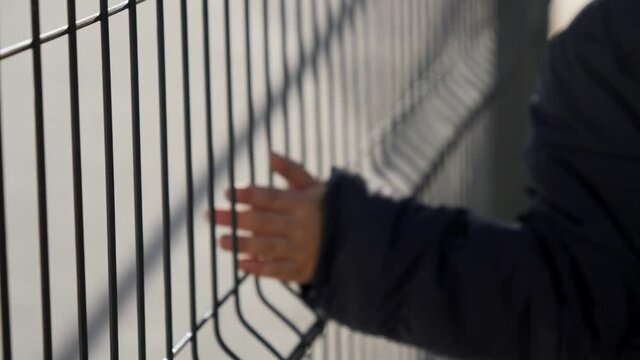 Little boy holding metal fence with hands. Concept of poverty, immigration, bullying and kids stress