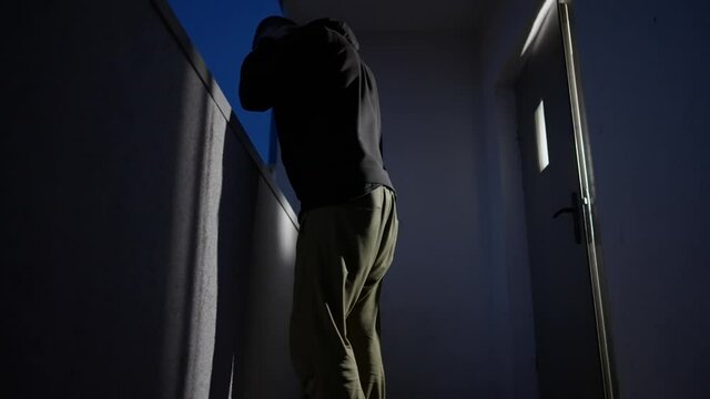 Hooded man looking aver a balcony balustrade at night