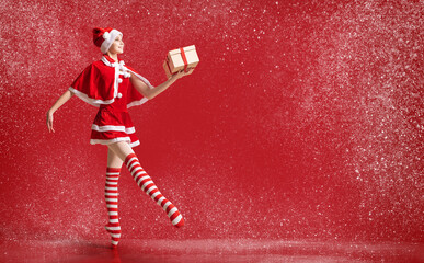 Dancing ballerina girl in pointe shoes with a gift in her hands dressed as Santa Claus on a red...