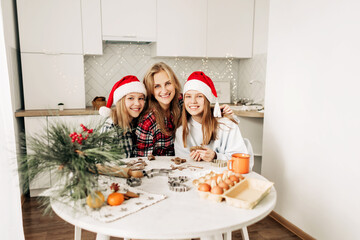 Portrait of a charming mother and her two lovely daughters while making Christmas gingerbread and cookies. Family tradition, time together, preparation for the holidays