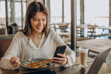 Young business woman having lunch in a cafe and working on computer