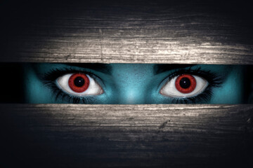 Scary, not human look through a crack in the dark with red eyes
