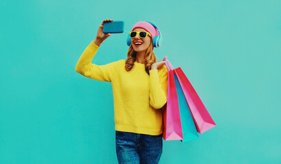 Stylish happy smiling woman taking a selfie by phone in headphones with shopping bags wearing a...