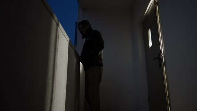 Furtive man in hoodie standing outside apartment door at night