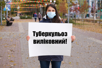 A masked woman holds a poster with text in Ukrainian, translated from Ukrainian - Tuberculosis is...