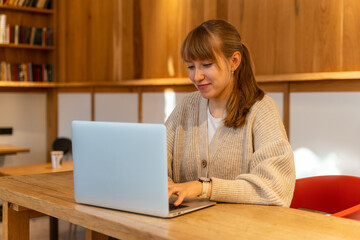 Young happy female using laptop in cafe. Remote work far from home. Horizontal