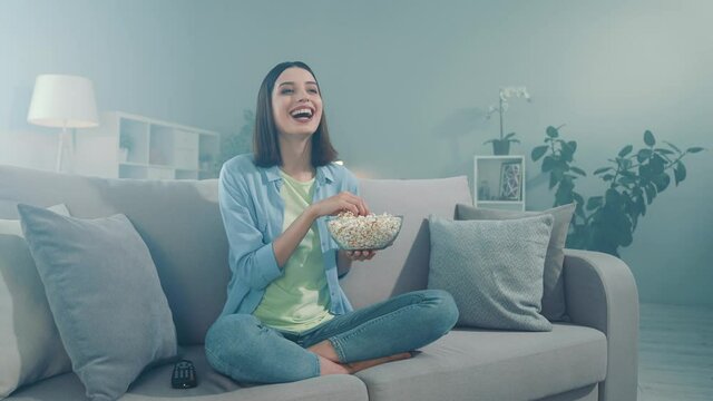 Excited lady sit divan look series laughter eat pop corn bowl in room