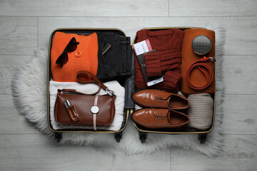 Open suitcase with folded clothes, accessories and shoes on floor, top view