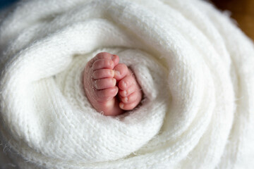 a small leg of the newborn in a white scarf. soft focus