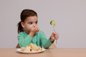 Cute little girl closing nose and refusing to eat vegetable salad at table on grey background