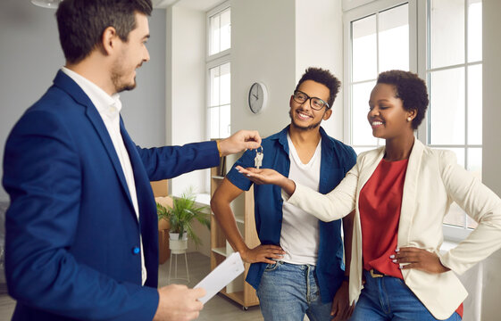Real estate agent gives house keys to young married black couple. Happy ethnic boyfriend and girlfriend or husband and wife meeting with realtor to make a deal and take keys to their new apartment