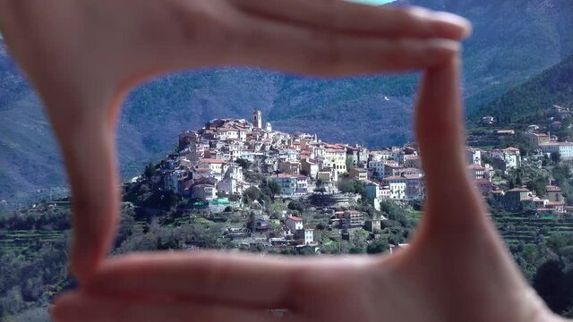 Finger Frame. Woman folding her hands in frame with ancient town of Perinaldo high in the mountains of Liguria in Western Italy
