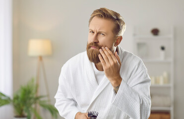 Good looking man doing morning skin and hair care routine. Handsome guy in white bathrobe looking...