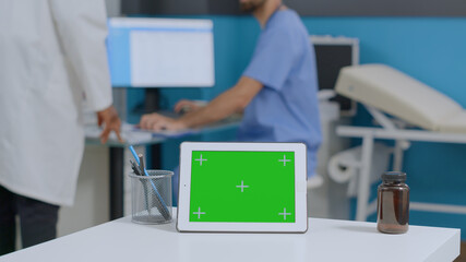 Naklejka na ściany i meble Closeup of mock up green screen chroma key tablet computer with isolated display standing on desk in hospital office. Multiethnic medical team analyzing sickness report working at healthcare treatment