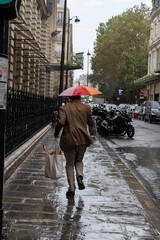 Monsieur courant avec le parapluie multicolor de son enfant pour braver la météo dans une rue typique parisienne.