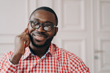 Smiling cheerful African man freelancer guy talking on mobile phone while working remotely