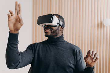 Smiling african american businessman in VR glasses sits in office, testing virtual reality goggles