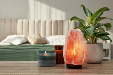 Beautiful Himalayan salt lamp, green plant and candles on wooden table in bedroom, space for text - obrazy, fototapety, plakaty