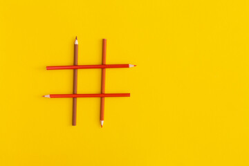 Hashtags sign made of colored pencils on yellow background