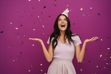 Young brunette woman in party cone making fun with confetti