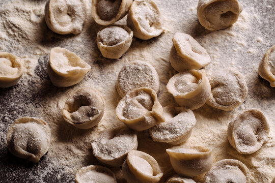 Lots of homemade dumplings on table with flour. Raw ravioli are ready for cooking. Close-up, selective focus.