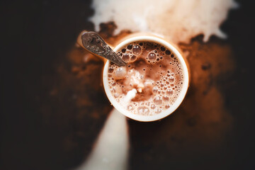 Top view of a mug of hot fragrant cocoa, into which cold milk is poured. The process of making a...