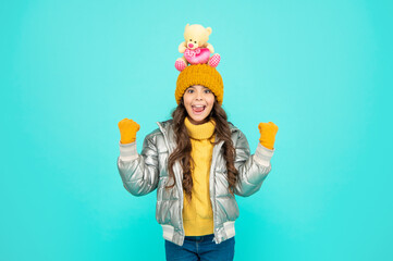 surprised teen girl in winter clothes hold toy on blue background, gift