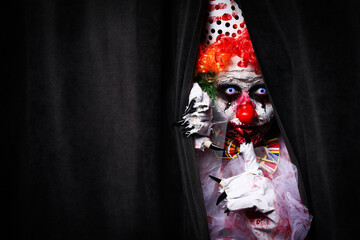 Terrifying clown hiding behind black curtains, space for text. Halloween party costume - obrazy, fototapety, plakaty