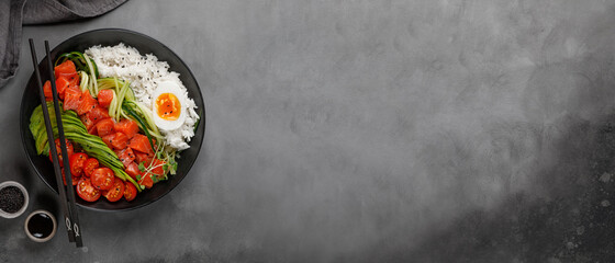 Banner Top view of poke bowl with salmon, avocado and rice on dark background with chopsticks