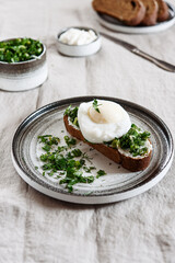 Healthy Breakfast with Poached Egg on toast with cream cheese and chopped mix of green onions, dill and parsley on greige linen tablecloth
