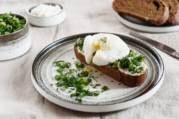 Healthy Breakfast with Poached Egg on toast with cream cheese and chopped mix of green onions, dill and parsley on greige linen tablecloth
