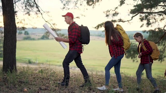 Family tourism. Group of people with map hiking in forest. People with backpacks in forest park. Hiking is healthy lifestyle. Group of ice is walking with map in forest park. Family tourism concept