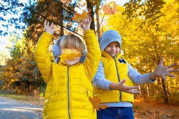 Two happy children throw leaves in the autumn park